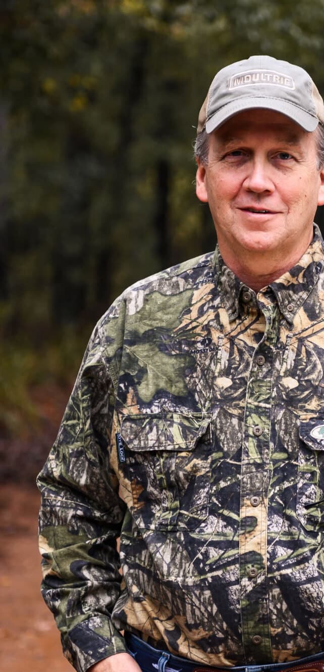 Man dressed in camo standing on a trail in the woods