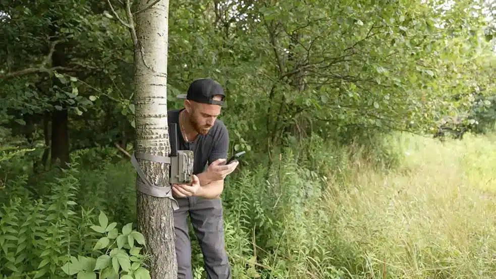 A person setting up a Moultrie Mobile Edge Camera in the woods.
